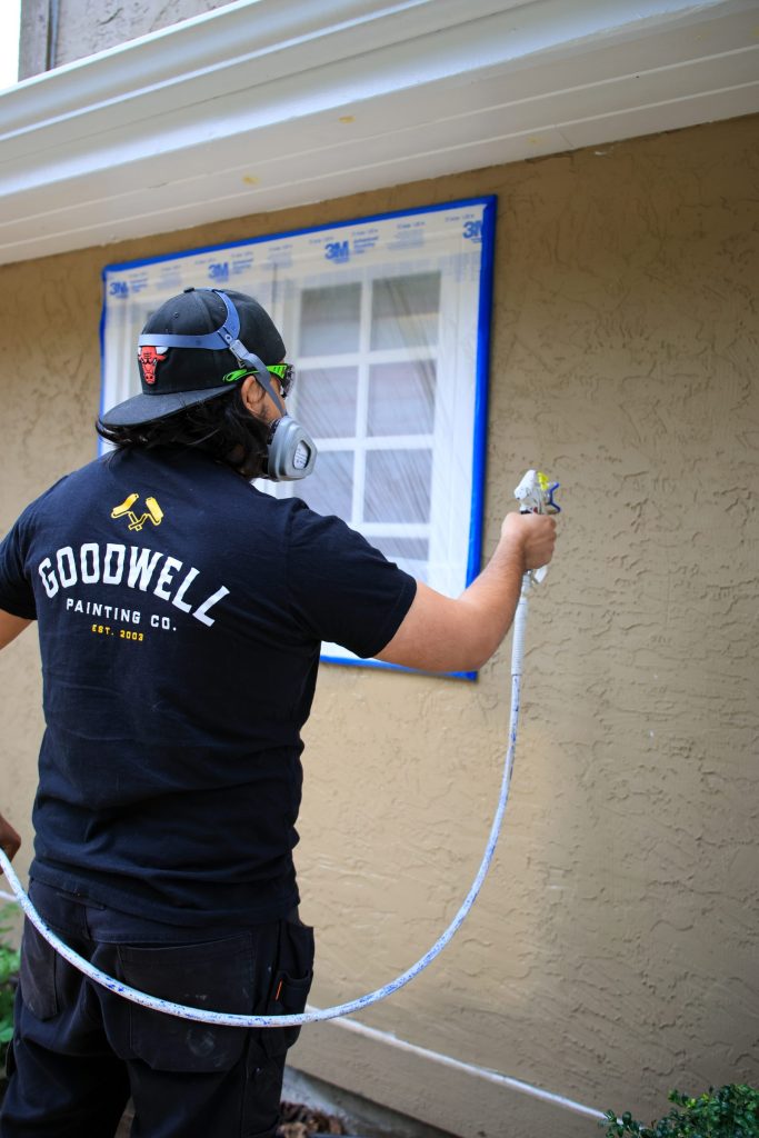 A Goodwell painter spraying exterior siding