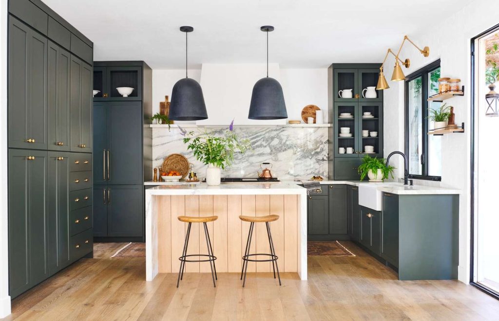 A refinished kitchen with deep green cabinets, brass hardware and a wood island