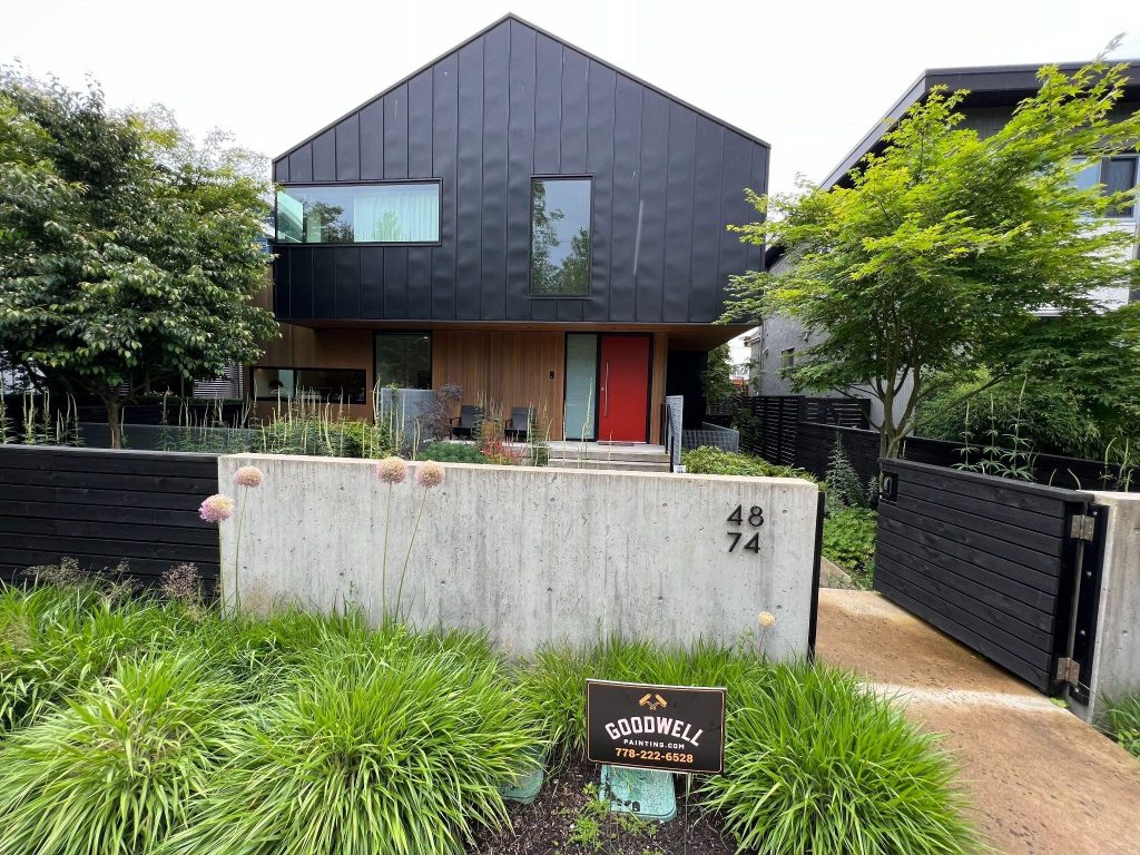A modern black-clad home in South Surrey with a Goodwell Painting sign out front