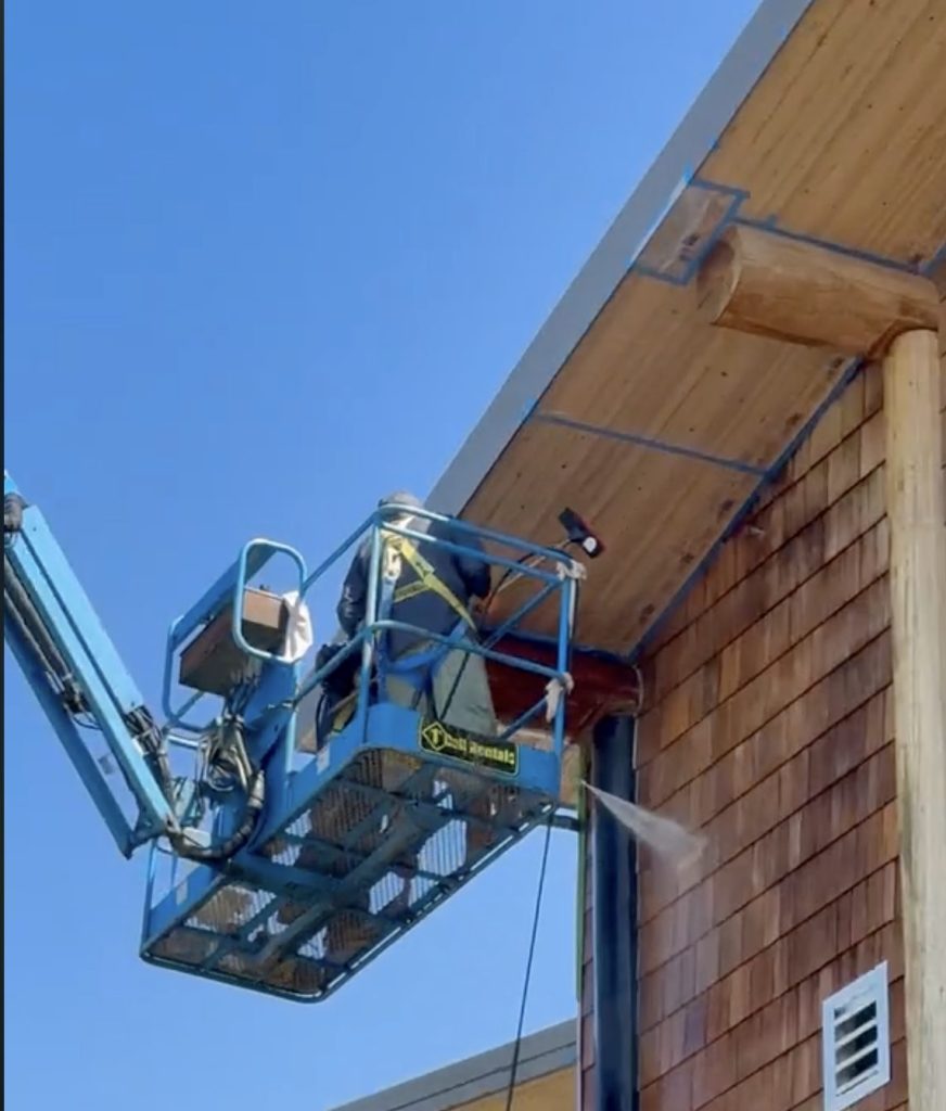 A Goodwell painter pressure washing cedar siding and soffits from a lift